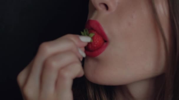 Крупный план: Сексуальная молодая девушка с красной помадой, поедающая клубнику, наслаждающаяся вкусом на черном фоне — стоковое видео