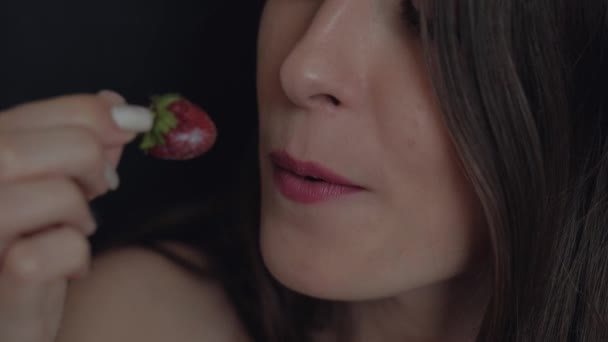 Décryptages Bouche de joyeuse jeune fille au rouge à lèvres mangeant des fraises à la crème blanche jouissant du goût sur fond noir — Video