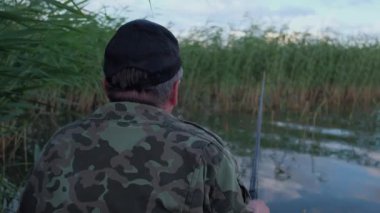 Arkadan Görünüm balıkçı bir tekne içinde bir şeyler yemek için bekleyen bir tekne içinde oturan kamuflaj içinde bir balık, ihtiyar yakalar
