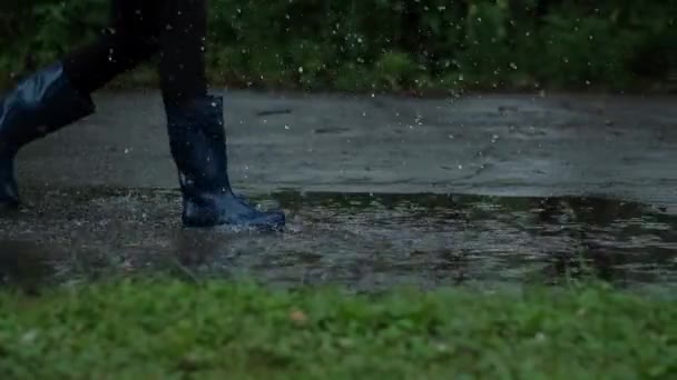 Gros plan - Fille en bottes en caoutchouc bleu qui court à travers les flaques d'eau, Gouttes d'eau éclaboussure efficace, Mouvement lent — Video