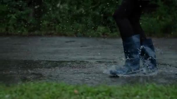 Gros plan - Fille en bottes en caoutchouc bleu qui court à travers les flaques d'eau, Gouttes d'eau éclaboussure efficace, Mouvement lent — Video