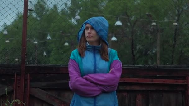 Portret van een meisje in de regen in een kleur regenjas, op de achtergrond van het oude stadion — Stockvideo