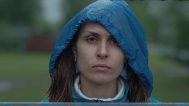 Closeup Portrait, menina de olhos azuis com capuz azul em pé na chuva, olhando penetrantemente para a câmera — Vídeo de Stock