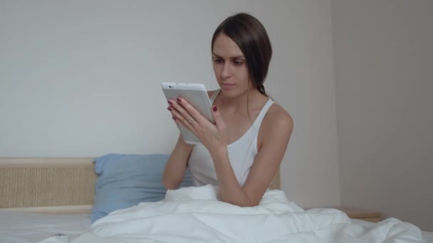 Gut aussehende Brünette mit einem Tablet in ihrem Schlafzimmer — Stockvideo