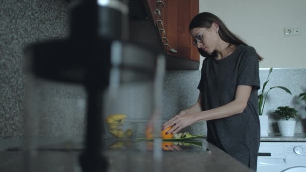 Θηλυκό ετοιμάζει πρωινό το πρωί στην κουζίνα. Μια γυναίκα κόβει φρούτα, πορτοκαλί στο τραπέζι. — Αρχείο Βίντεο