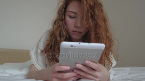 Chica de pelo rojo bien parecido con una tableta digital en su dormitorio — Vídeos de Stock