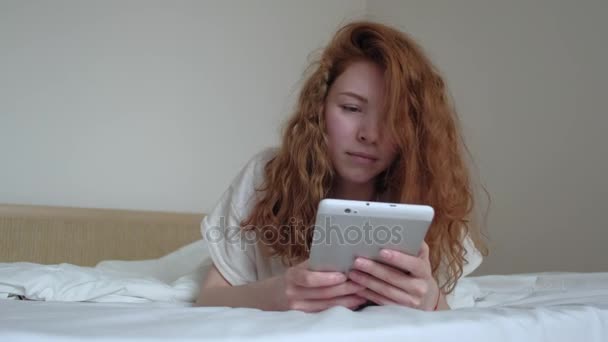 Bella ragazza dai capelli rossi con un tablet digitale nella sua camera da letto — Video Stock