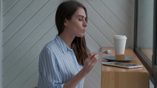 Mujer en la cafetería bebiendo café con leche caliente, comiendo rebanada de pastel de queso . — Vídeo de stock