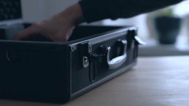 Adamın elleri siyah kutuya bir nesne koyar ve çantayı alıp gider..