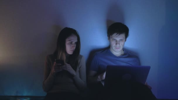 Young couple sits at night, using their electronic devices, communicate. — Stock Video