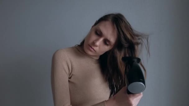 Mujer atractiva secando el cabello usando secador de pelo negro sobre fondo de pared blanco . — Vídeos de Stock