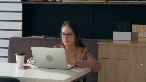 Hermosa mujer en gafas de uso portátil y beber café en la cafetería . — Vídeos de Stock