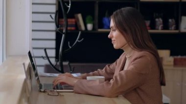 Güzel bir kadın kahve dükkanında dizüstü bilgisayar kullanır ve kahve içer..