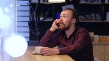 Bir adam telefonda bir arkadaşıyla ya da meslektaşıyla konuşuyor ve kahve içiyor..