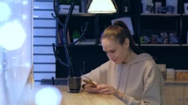 Bir gece kafesinde akıllı telefon kullanan, kahve içen genç bir kadın..