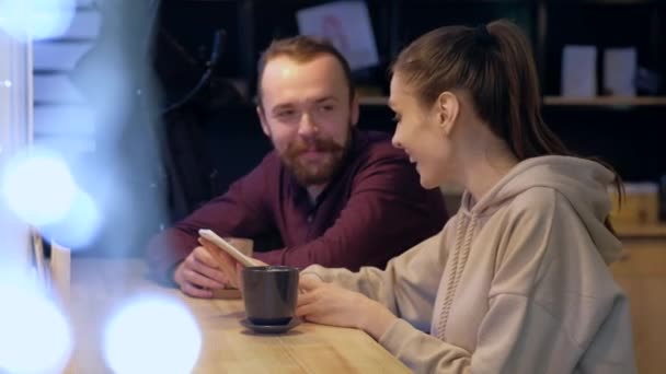 Ett par sitter i ett café, pratar, dricker kaffe och tittar på i smartphone. — Stockvideo