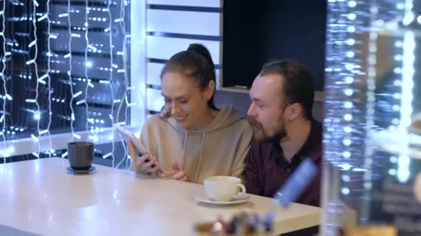 Ett par sitter i ett café, pratar, dricker kaffe och tittar på i smartphone. — Stockvideo
