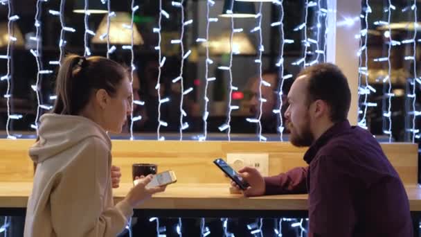 Пара сидить у кафе, розмовляє, п'є каву та користується смартфоном . — стокове відео