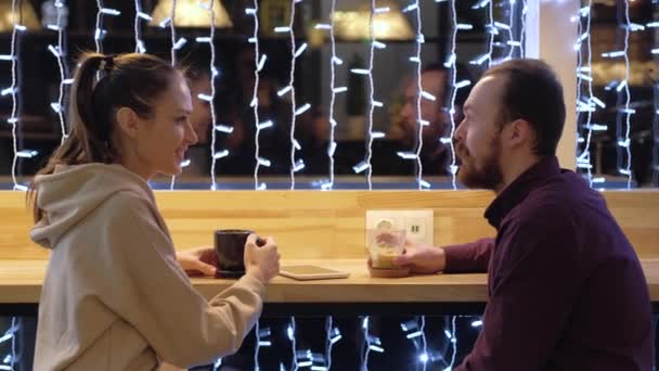 Ein Paar sitzt in einem Café, redet, trinkt Kaffee und benutzt ein Smartphone. — Stockvideo