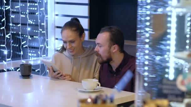 Ett par sitter i ett café, pratar, dricker kaffe och tittar på i smartphone. — Stockvideo