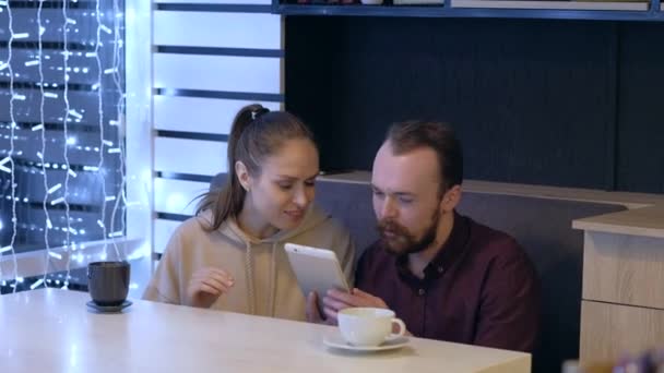 Um casal sentado em um café, conversando, bebe café e assistindo em smartphone . — Vídeo de Stock