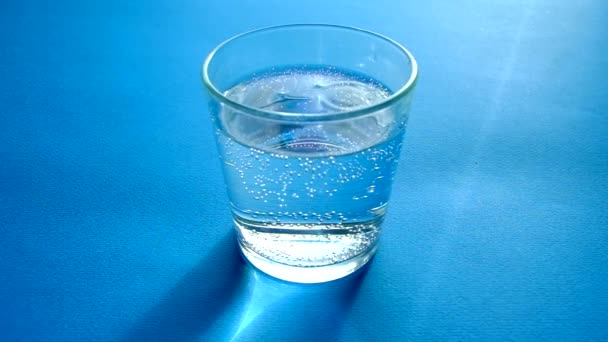 Effacer l'eau gazeuse dans un verre transparent sur un fond bleu . — Video