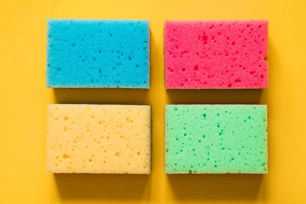 Yellow, green, red, blue sponges on colored paper background, top view.