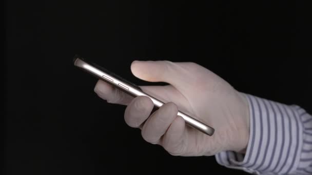 黒の背景にスマートフォンを保持滅菌医療用手袋の女性の手 コロナウイルス菌に対する保護の概念 — ストック動画