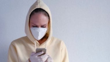 Koruyucu maske takan bir kadın cep telefonu kullanıyor. Beyaz arka planda izole edilmiş. Kendilerini korona virüsü enfeksiyonundan koruyorlar..