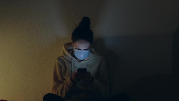 Koruyucu Maskeli Bir Kadın Akşam Karantina Sırasında Akıllı Telefonuyla Evde — Stok video