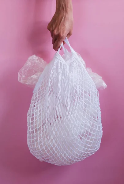 Plastic bags in a string bag on pink background.