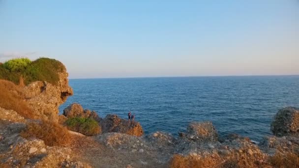 Två killar traveler stående på klipporna vid kusten — Stockvideo
