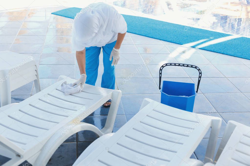 worker at the hotel removes the water from the deck chairs after the rain