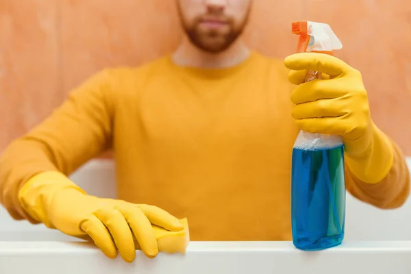 Homem limpa banheiro com esponja e produtos de limpeza — Fotografia de Stock