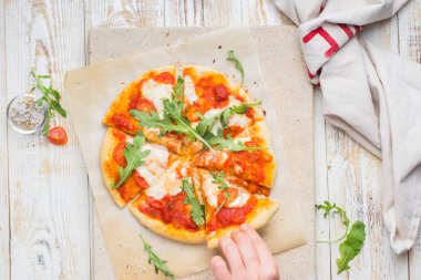 Napolice pizza domates, mozzarella peyniri, roka hafif bir taş ve ahşap bir arka plan ile. nefis.) Düz yatıyordu, en iyi görünüm. Elleri ile gıda fotoğraf.