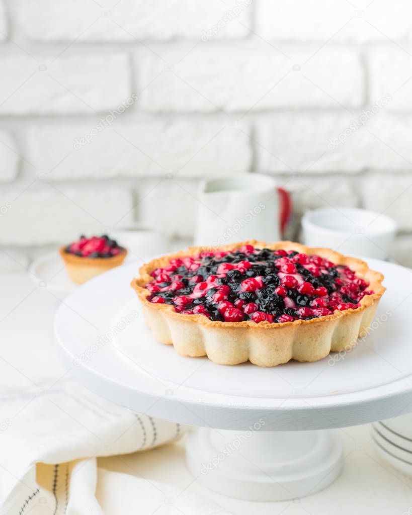 Tart  with cream and berries in a cafe. A modern cake with a cut piece. Light background, white brick wall, light dishes and cake stand. The atmosphere of the coffee house. 