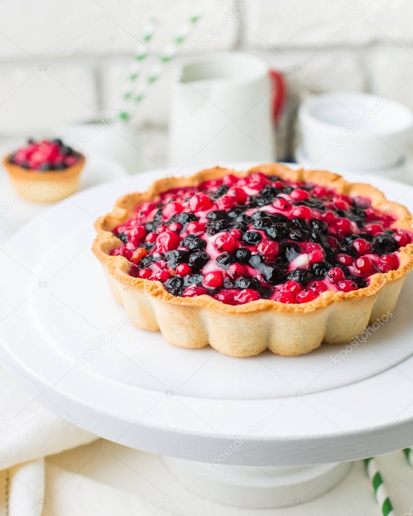 Tart  with cream and berries in a cafe. A modern cake with a cut piece. Light background, white brick wall, light dishes and cake stand. The atmosphere of the coffee house. 