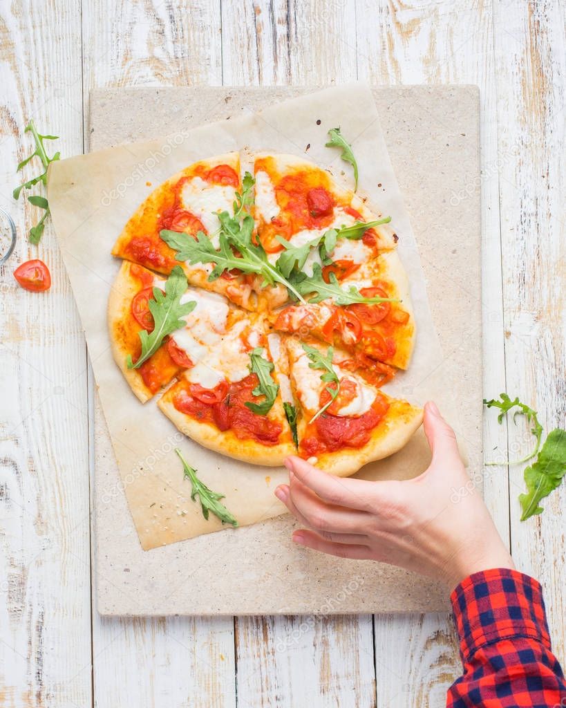 Neapolitan pizza with tomatoes, mozzarella, arugula on a light stone and a wooden background. yummy.)Flat lay, top view. Food photo with hands.