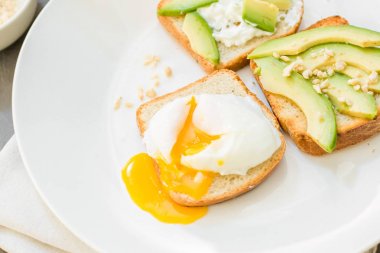 Kahvaltı. Yumurta tost avokado, beyaz peynir, baharat ve kuruyemiş. Beyaz tabak, gri beton arka plan.