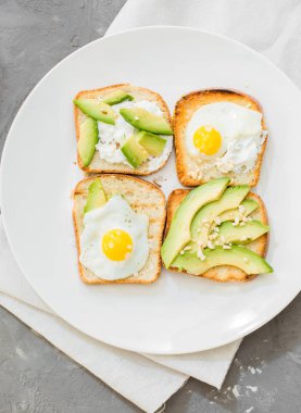 Kahvaltı. Yumurta tost avokado, beyaz peynir, baharat ve kuruyemiş. Beyaz tabak, gri beton arka plan.
