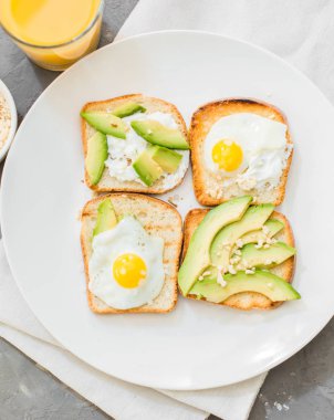 Kahvaltı. Yumurta tost avokado, beyaz peynir, baharat ve kuruyemiş. Beyaz tabak, gri beton arka plan.