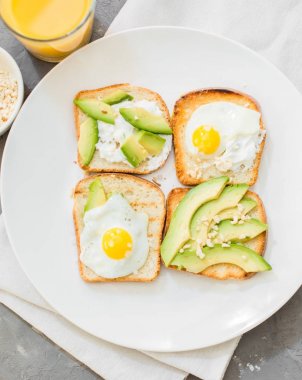 Kahvaltı. Yumurta tost avokado, beyaz peynir, baharat ve kuruyemiş. Beyaz tabak, gri beton arka plan.