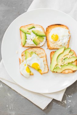 Kahvaltı. Yumurta tost avokado, beyaz peynir, baharat ve kuruyemiş. Beyaz tabak, gri beton arka plan.