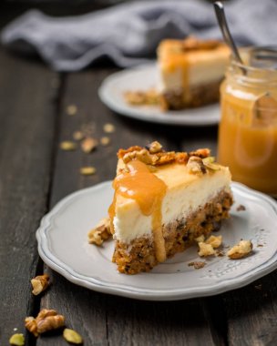 Carrot nut vanilla cheesecake with salty homemade caramel on a white plate on a dark wooden vintage background. Two pieces of homemade cheesecake. Caramel sauce in a jar. clipart