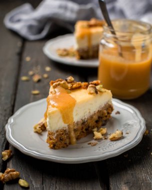 Carrot nut vanilla cheesecake with salty homemade caramel on a white plate on a dark wooden vintage background. Two pieces of homemade cheesecake. Caramel sauce in a jar. clipart