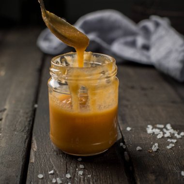 Bir kavanoz içinde karamel sos. Koyu ahşap antika arka plan beyaz bir tabağa tuzlu ev yapımı karamel ile havuç somun vanilyalı cheesecake. İki adet ev yapımı cheesecake. 