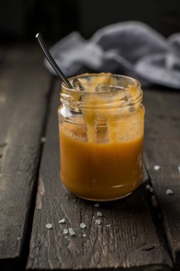 Bir kavanoz içinde karamel sos. Koyu ahşap antika arka plan beyaz bir tabağa tuzlu ev yapımı karamel ile havuç somun vanilyalı cheesecake. İki adet ev yapımı cheesecake. 