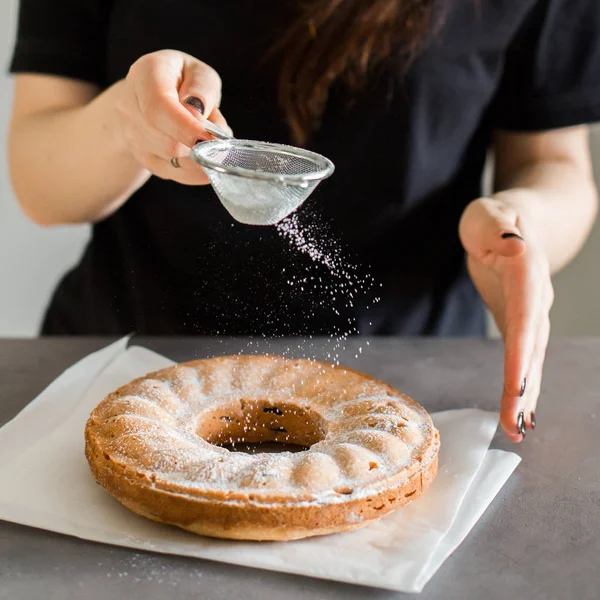 The process of baking the cake. Sugar powder, beautifully flying in the sunlight, falls on a warm homemade cake.