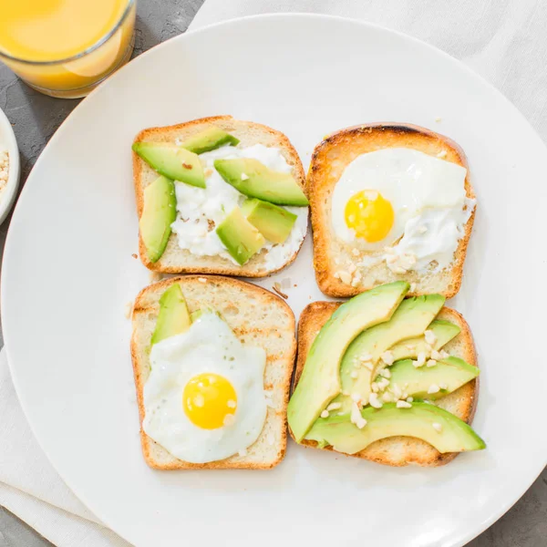 Kahvaltı. Yumurta tost avokado, beyaz peynir, baharat ve kuruyemiş. Beyaz tabak, gri beton arka plan.