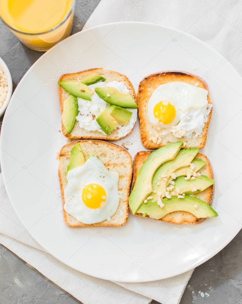 Breakfast. Eggs on toast with avocado, soft white cheese, spices and nuts. White plate, gray concrete background.